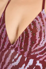 Malla enteriza con estampado animal print tipo cebra en tonos bordó y rosado, con diseño triangular y tirantes ajustables al cuello. Presenta detalles de tachas aplicadas en el busto.