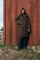 Campera larga acolchonada color marrón, con diseño midi, capucha amplia, cierre frontal con cremallera y broches, y bolsillos delanteros con tapa.
