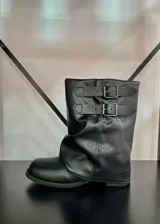 Botas de caña baja color negro, con diseño holgado y dos correas decorativas con hebillas metálicas en la parte superior.