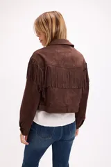 Chaqueta de efecto gamuza en color marrón, con diseño de inspiración western que presenta flecos en la parte frontal y en la espalda. Cuenta con cuello clásico, cierre frontal con botones metálicos a presión y mangas largas.