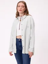 Camisa de corte oversize con diseño a rayas verticales en tonos azul y blanco. Presenta cuello clásico, cierre frontal con botones y un bolsillo en el pecho con detalle de etiqueta.