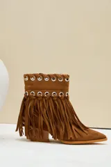 Bota texana de gamuza color camel, con taco cuadrado y punta fina. Cuenta con flecos largos colgantes y detalles de ojalillos metálicos plateados en la parte superior.