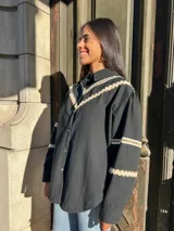 Camisa blanca de mangas largas con detalles de puntilla beige en cuello y puños, y cierre frontal con botones.