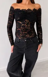 Top de encaje negro con diseño off-shoulder, mangas largas y detalle fruncido en el centro del busto.