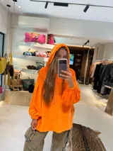 Buzo oversize de plush color naranja, con capucha ajustable por cordones, bolsillo canguro delantero y mangas largas abullonadas con puños elásticos.