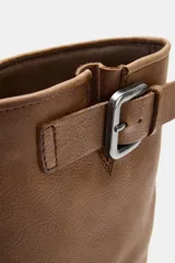 Bota de piel color marrón de caña alta, con detalle de hebilla metálica en la parte superior, efecto desgastado y suela dentada negra.