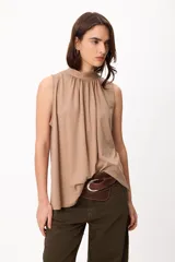 Blusa sin mangas color crema, con cuello alto fruncido y diseño holgado.