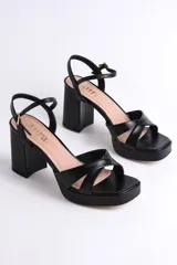 Sandalias negras de cuero sintético con plataforma y tacón cuadrado. Presentan tiras cruzadas en el empeine y pulsera con hebilla al tobillo.