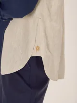 Camisa de lino color blanco con detalles combinados en tonos beige, cuello camisero, cierre frontal con botones oscuros y mangas largas con puños en contraste.