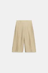 Bermuda de tiro alto color beige con trabillas en la cintura y detalle de pliegues en la parte delantera. Presenta un corte amplio y largo por debajo de las rodillas.