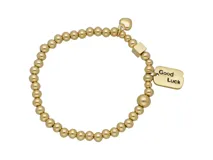 Pulsera elástica de acero dorado con bolitas y dijes colgantes: un corazón y una chapa rectangular con la inscripción "Good Luck".