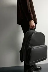 Mochila negra con acabado texturizado, compartimento principal con cierre de cremallera y bolsillo frontal con cremallera. Incluye parte posterior acolchada, asa de mano superior y dos asas de hombro ajustables.