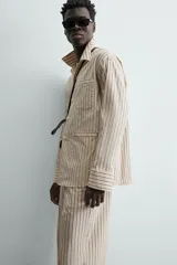 Camisa de calce relajado con diseño de rayas verticales, cuello bowling y manga larga. Cuenta con cierre frontal de botones y tres bolsillos de plastrón: uno en el pecho y dos en la cadera.