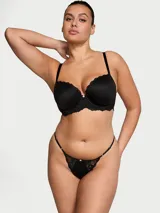 Bombacha tipo tanga de tiro bajo en color negro, confeccionada en microfibra ultrasuave con detalles de encaje en los laterales y ribetes. Cuenta con tiras laterales ajustables con herrajes dorados y un pequeño detalle de roseta en el centro.