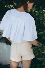Short de tiro alto en denim de algodón levemente elástico, color beige, con bolsillos delanteros de parche con ribete y cierre frontal con botón.