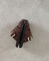 Zueco tipo sandalia de estilo jaula, confeccionado en gamuza negra con tiras entrelazadas y hebilla metálica dorada lateral. Cuenta con plantilla acolchada con logo de la marca.