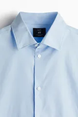 Camisa de manga larga color celeste claro, con cuello italiano y tapeta lisa con botones blancos. Presenta un corte ajustado (slim fit) y bajo redondeado.