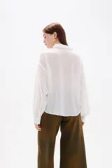 Camisa de color blanco con textura de pequeños puntos en relieve, cuello clásico, cierre frontal con botones y mangas largas con detalle de punto smock y puños elásticos.