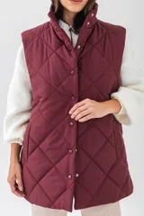 Chaleco acolchado negro con diseño de rombos, cuello alto y cierre frontal con botones a presión. Cuenta con bolsillos laterales.