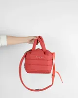 Bolso pequeño de mano color rojo ladrillo, con diseño acolchado horizontal y correa larga ajustable al hombro.