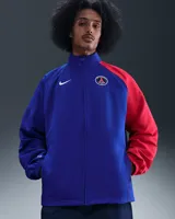 Campera deportiva Nike del Paris Saint-Germain, modelo Total 90 Reissue 2004, de color azul con una de las mangas en color rojo. Cuenta con cierre frontal completo, cuello alto y bolsillos laterales.
