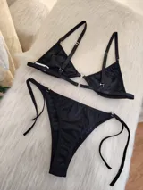 Conjunto de bikini color negro con textura acanalada. El corpiño es de estilo triangular con aros y detalle de argolla metálica en el centro. La bombacha es de corte colaless con tiras laterales ajustables y detalles de argollas metálicas.