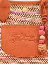 Bolso tipo cesta de tamaño XS, confeccionado en tejido de paja con detalles en cuero color naranja. Cuenta con asas cortas, correa larga ajustable y cierre de botón a presión con solapa de cuero grabada.