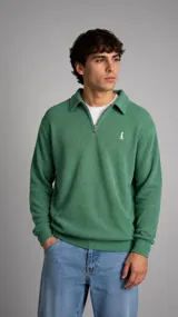 Buzo de punto color verde con cuello polo y cierre frontal parcial. Presenta textura acanalada, mangas largas con puños elásticos y un pequeño logo bordado en el pecho.