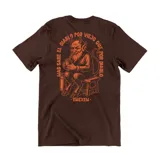 Remera marrón de algodón con estampa en color naranja en la espalda que muestra a un diablo tomando mate sentado en un banco, con la frase 'Más sabe el diablo por viejo que por diablo'.