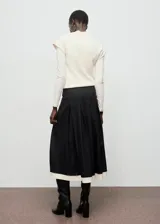 Falda midi evasé de tiro medio color negro, con diseño de tablas y detalle de vivo en el borde inferior. Cuenta con cierre de cremallera lateral.