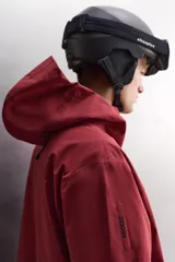 Cazadora deportiva de esquí con diseño bicolor en tonos negro y verde oliva. Presenta capucha amplia con visera, cierre frontal con cremallera termosellada, bolsillos frontales y en manga con cierres impermeables, y aberturas de ventilación en las axilas. Incluye faldón interior antinieve, puños ajustables y tecnología de rescate RECCO.