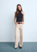 Pantalón de jean estilo wide leg color beige, con tiro alto, cierre frontal de cremallera y botón, y dos bolsillos de parche en la parte delantera.