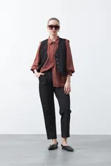 Camisa negra de estilo sastrero con cuello clásico, frente abotonado y mangas largas con puños ajustados. Presenta un diseño con hombreras sutiles que aportan estructura a la prenda.