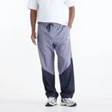 Pantalón New Balance de hombre, modelo Sport Legacy, con diseño de bloques de color en gris y azul marino. Cuenta con cintura elástica con cordón de ajuste, bolsillos laterales y el logo de la marca bordado en la pierna izquierda.