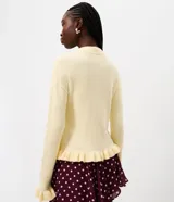 Suéter de tricot color amarillo claro, de manga larga y cuello redondo. Presenta detalles de volados acanalados en el ruedo y en los puños.