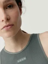 Musculosa de tejido acanalado color verde militar, con cuello redondo alto y diseño al cuerpo. Presenta una pequeña etiqueta decorativa en el centro del pecho.