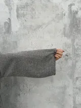 Polera de punto acanalado en color gris, con diseño de cuello abierto lateral, corte recto y mangas amplias.