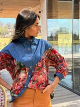 Camisa oversize combinada que mezcla denim azul en la parte superior y mangas, con tela vintage de estampado geométrico y tribal multicolor en la espalda y mangas. Presenta cuello camisero y corte holgado.