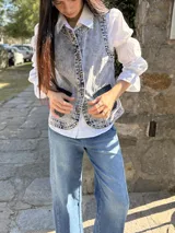 Chaleco de jean con efecto lavado, cierre frontal con botones metálicos y dos bolsillos cargo delanteros de cuero negro.