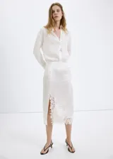 Falda midi de tiro medio color blanco, de corte recto con abertura lateral pronunciada y detalles de encaje en el borde y la abertura.