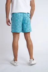 Short de baño con cintura elástica y cordón ajustable, confeccionado en tela ligera de secado rápido. Presenta un estampado botánico integral en tonos amarillos, blancos y azules, con dos bolsillos delanteros y uno posterior.