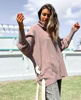 Polerón de cuello alto y corte oversize, color rosado, con mangas largas de puño acanalado y detalle de ojalillos metálicos con tiras en los laterales.