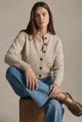 Cardigan de punto en tono beige melange con efecto jaspeado, de corte al cuerpo y manga larga. Presenta cierre frontal con botones oscuros y dos bolsillos delanteros aplicados.