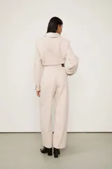 Enterito baggy de sarga color beige, de corte holgado, escote en V cruzado, manga larga y ajuste con lazo y hebilla en la cintura.
