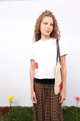 Remera blanca de corte oversize con cuello redondo y manga corta. Presenta un detalle de parche rectangular en color rojo en la parte inferior derecha.