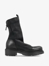 Bota corta de cuero negro con diseño minimalista, cierre lateral y suela robusta con relieve. Presenta un acabado ligeramente desgastado que le otorga una estética urbana y moderna.