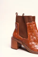 Bota tipo botineta de cuero negro con diseño trenzado artesanal en toda la capellada. Presenta paneles laterales elásticos, taco cuadrado de altura media y tirador en la parte superior trasera.