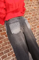 Jean de corte wide leg con diseño de paneles en diferentes tonos de gris y negro. Presenta cierre frontal expuesto y costuras decorativas que crean un efecto visual de bloques de color.