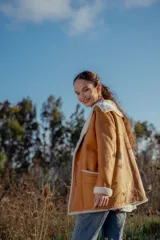 Campera gamulan color camel de cuero italiano con interior de piel sintética blanca. Tiene cuello solapa amplio, cierre con botones y bolsillos laterales.