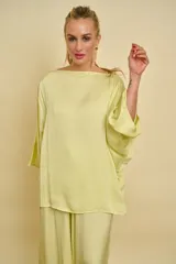 Blusa de satén de seda color verde claro, con cuello bote y mangas amplias tipo murciélago de corte holgado.